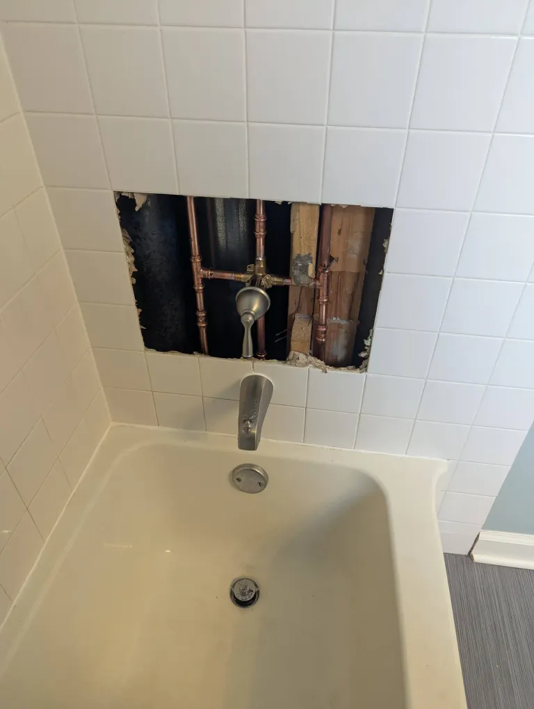 Tile removed around a tub faucet to expose brass pipes.