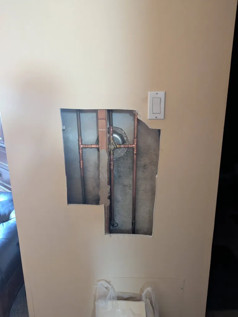 Drywall removed to expose brass pipes in a wall.