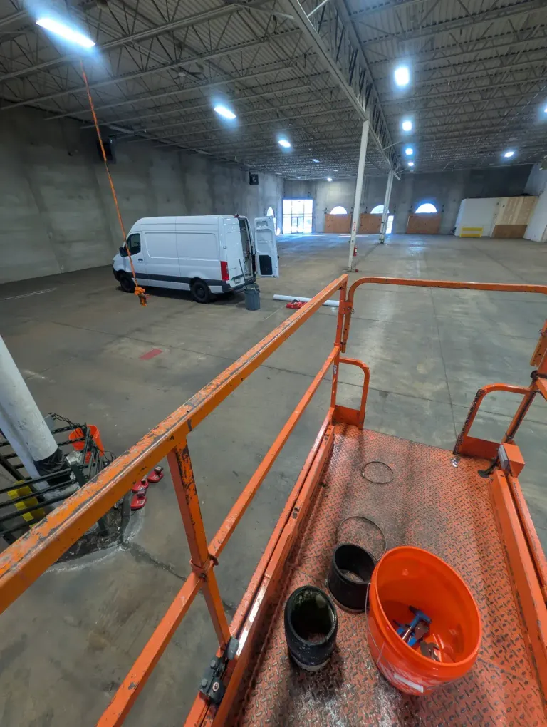Warehouse interior viewed from scaffolding during ceiling pipe work.