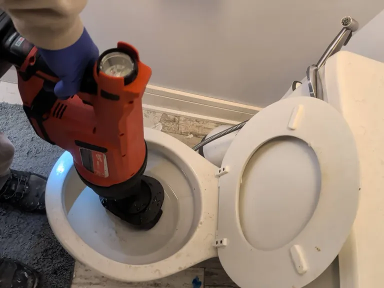 A powered drain tool seated in a toilet bowl to clear a clog.