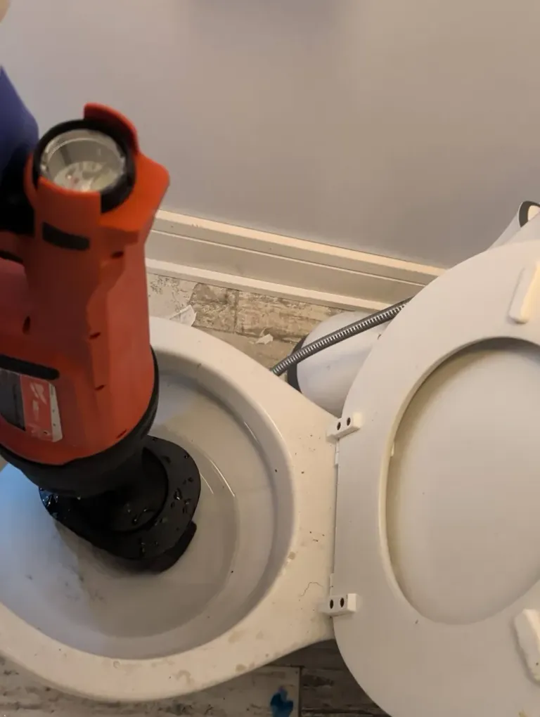 A powered drain tool seated in a toilet bowl to clear a clog.