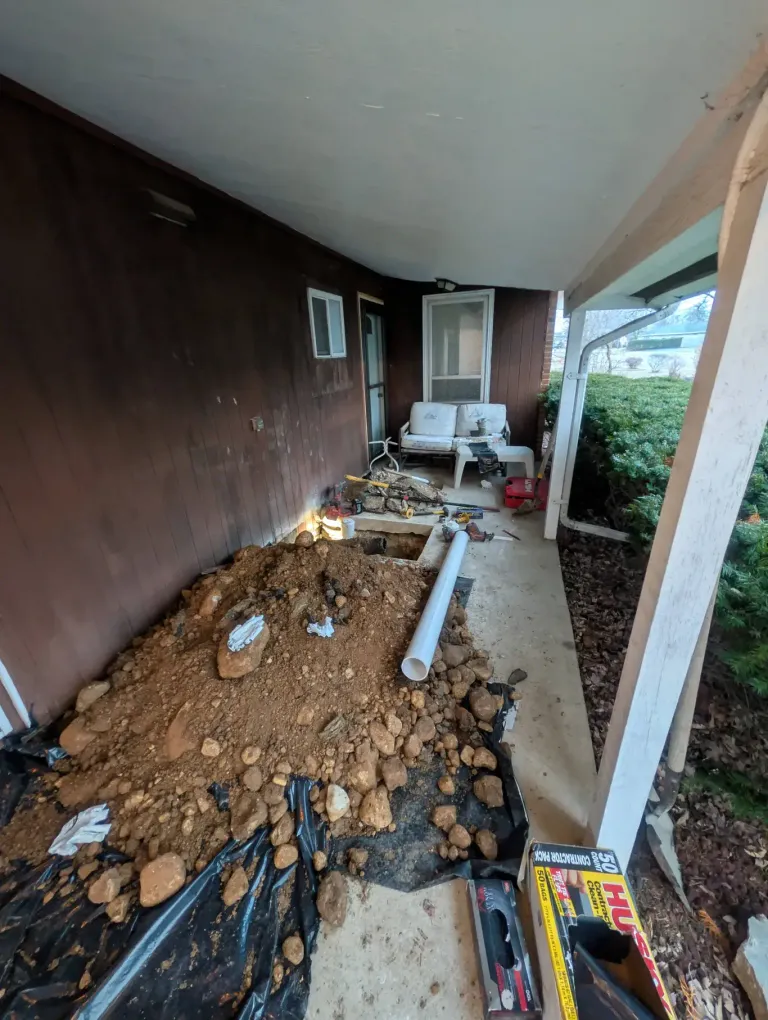 A patio slab opened for a dig, with PVC pipe staged beside the hole.