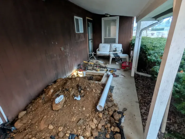 A patio slab opened for a dig, with PVC pipe staged beside the hole.