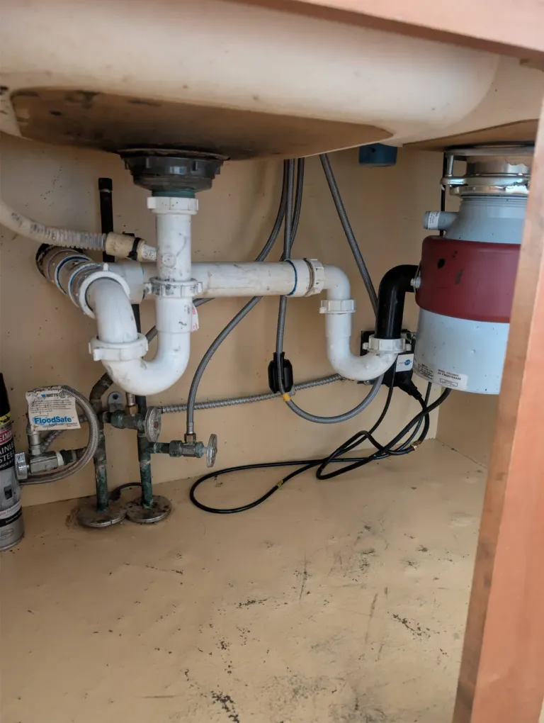 Under-sink pipes next to a garbage disposal.