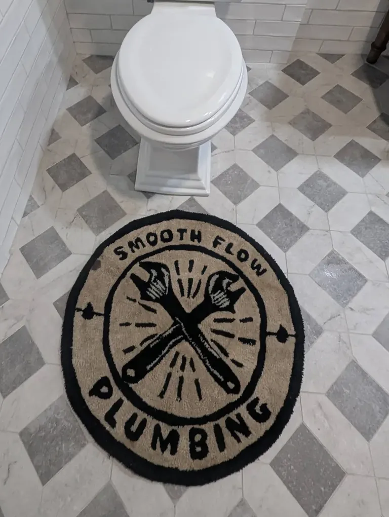A toilet with a Smooth Flow branded rug on the bathroom floor.